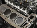Nowa uszczelka pod głowicę czeka na montaż. Widać cylindry i fragmenty silnika.