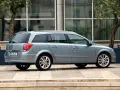 Srebrny Opel Astra H 1.6 benzyna kombi zaparkowany na tle nowoczesnego budynku z drzewami.
