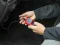 Ręce trzymające czerwony interfejs diagnostyczny OBDII/EOBD, podłączony do samochodu.