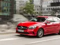 Czerwony Mercedes-Benz W176 pędzi ulicą miasta, mijając nowoczesne budynki.