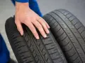 Dłoń mechanika dotyka bieżnika opony Hankook, sprawdzając jej stan. Dobre opony Hankook opinie to podstawa bezpiecznej jazdy.