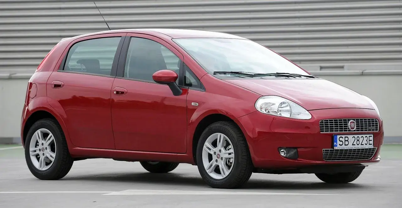 Czerwony Fiat Grande Punto, często chwalony w fiat grande punto opinie, stoi na szarym tle.