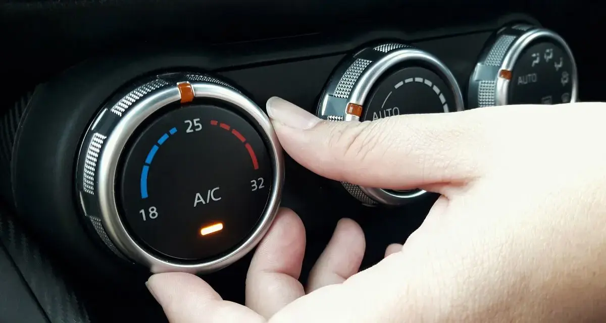 Dłoń reguluje pokrętłem temperaturę klimatyzacji w samochodzie, ustawiając ją na 25 stopni.