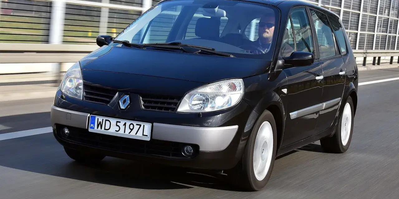 Czarny Renault Scenic 2 jedzie autostradą. Kierowca w okularach przeciwsłonecznych prowadzi auto.