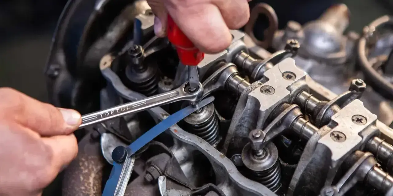 Mechanik reguluje luzy zaworowe silnika, używając klucza i szczelinomierza.