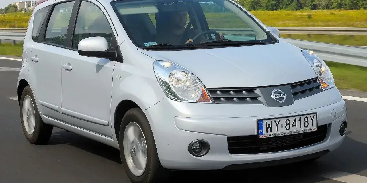 Srebrny Nissan Note E11 jedzie po drodze, za kierownicą siedzi mężczyzna.