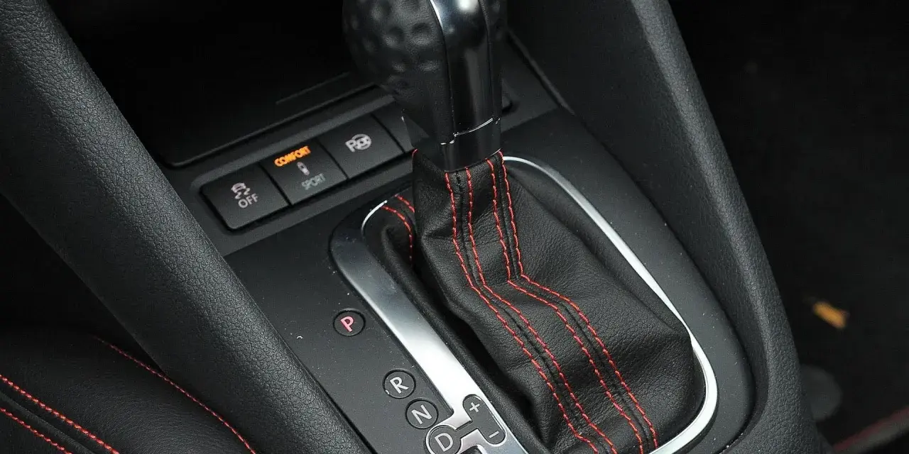 Zbliżenie na dźwignię automatycznej skrzyni biegów z oznaczeniami P, R, N, D, S. Widoczne przyciski trybów Comfort i Sport.