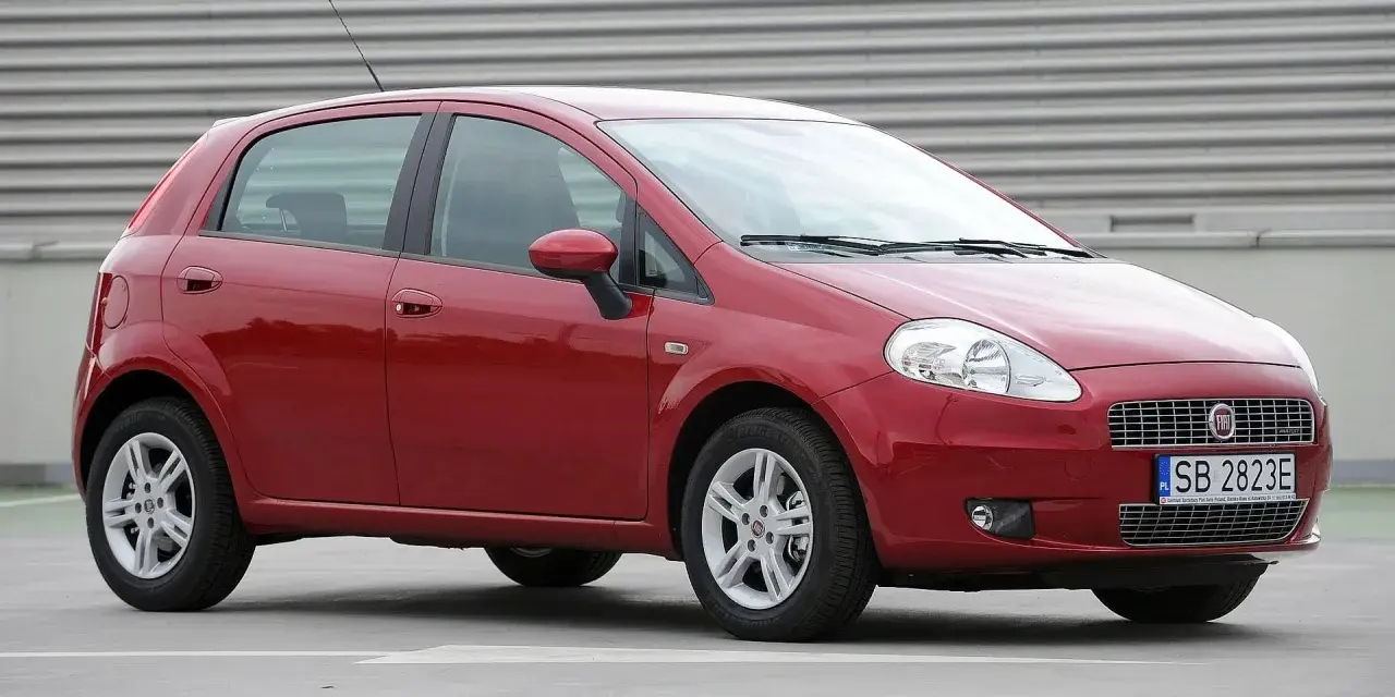 Czerwony Fiat Grande Punto, często chwalony w fiat grande punto opinie, stoi na szarym tle.