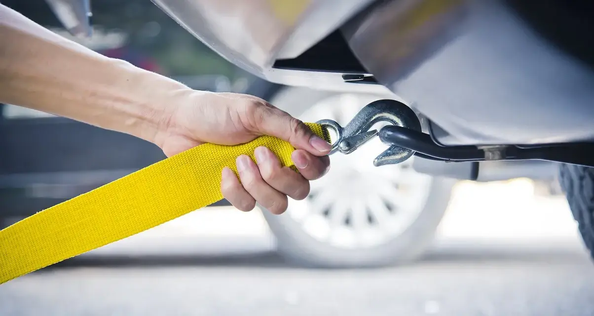 Dłoń mocuje żółtą linę holowniczą do haka. To kluczowy moment, jak holować auto, by bezpiecznie przetransportować pojazd.