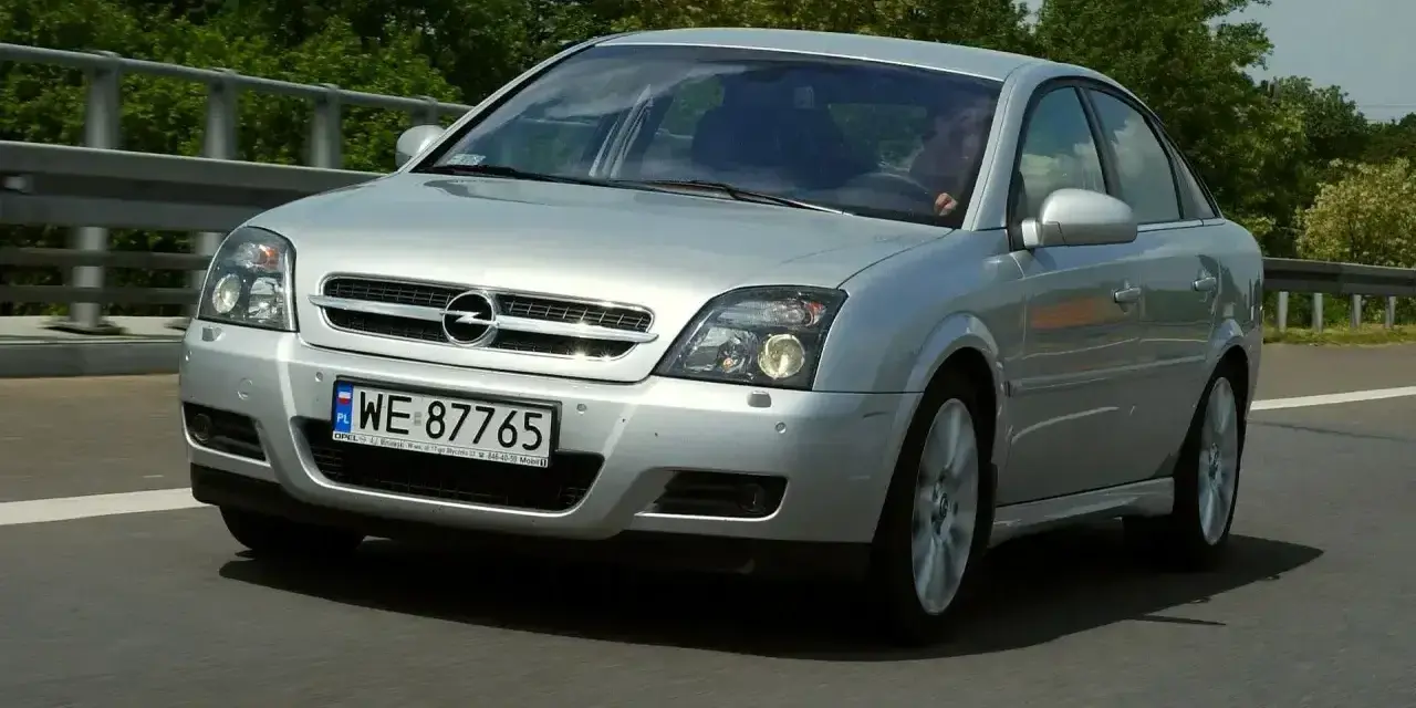 Srebrny Opel Vectra C GTS z polskimi tablicami WE 87765 jedzie po drodze, otoczony zielenią.
