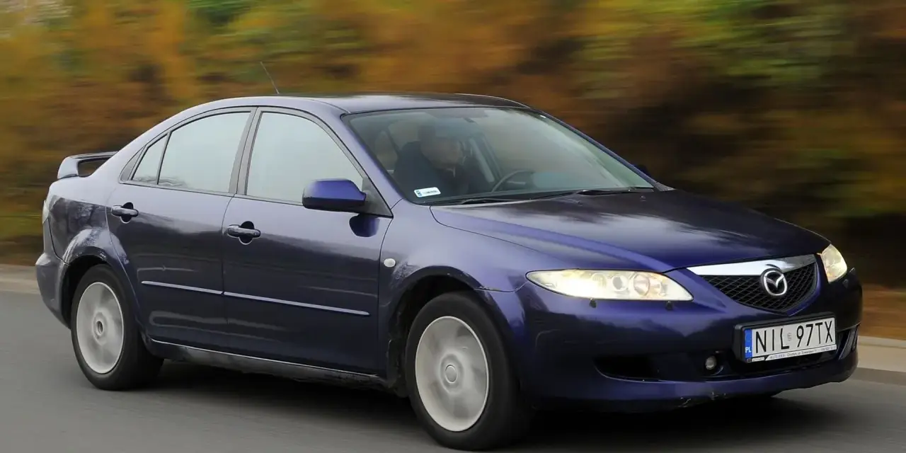 Granatowa Mazda 6 GG jedzie po drodze, za nią rozmyte drzewa w jesiennych barwach.