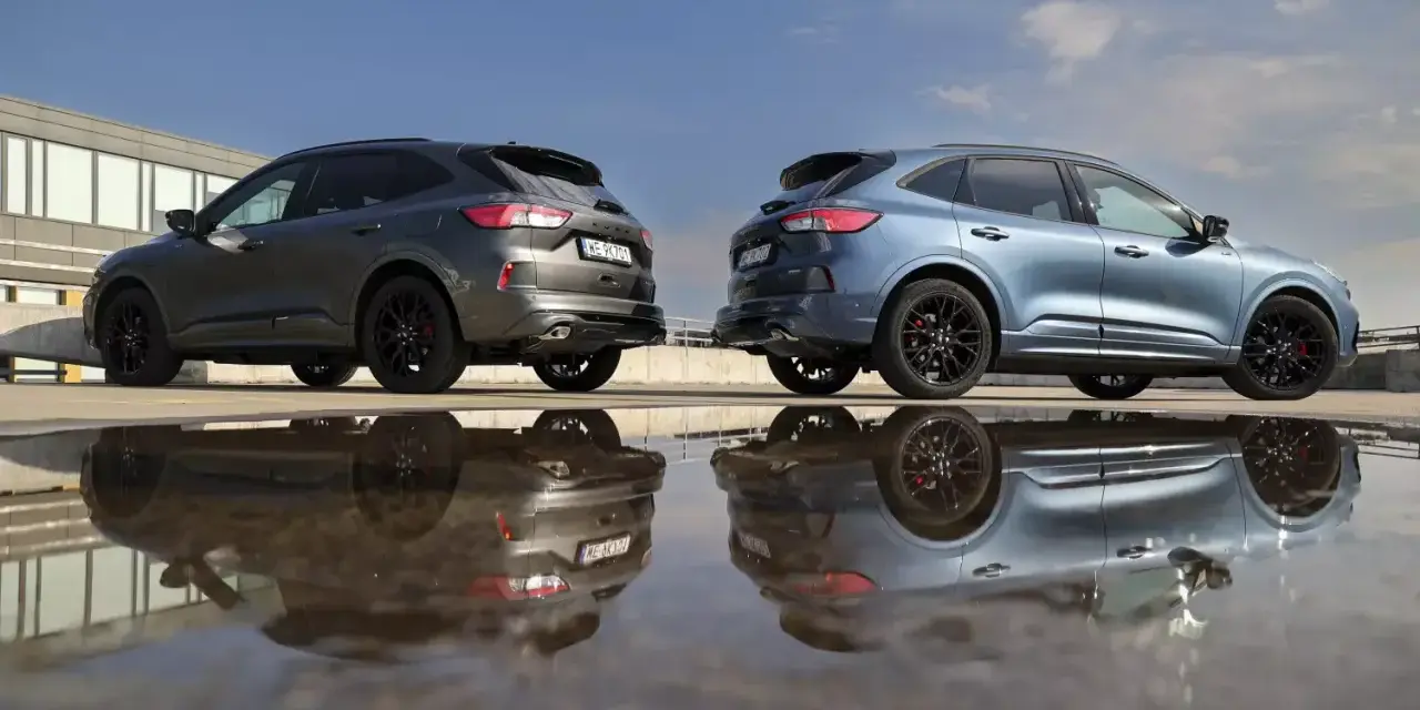 Dwa Fordy Kuga, jeden szary, drugi niebieski, stoją obok siebie na parkingu. Ich odbicia w kałuży tworzą surrealistyczny obraz. Oba modele to wersje hev.