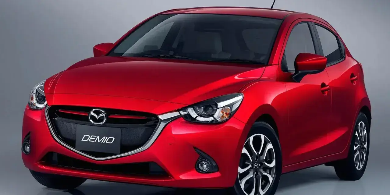 Czerwona Mazda Demio z błyszczącym grillem i reflektorami.
