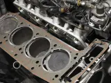Nowa uszczelka pod głowicę czeka na montaż. Widać cylindry i fragmenty silnika.