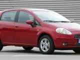Czerwony Fiat Grande Punto, często chwalony w fiat grande punto opinie, stoi na szarym tle.