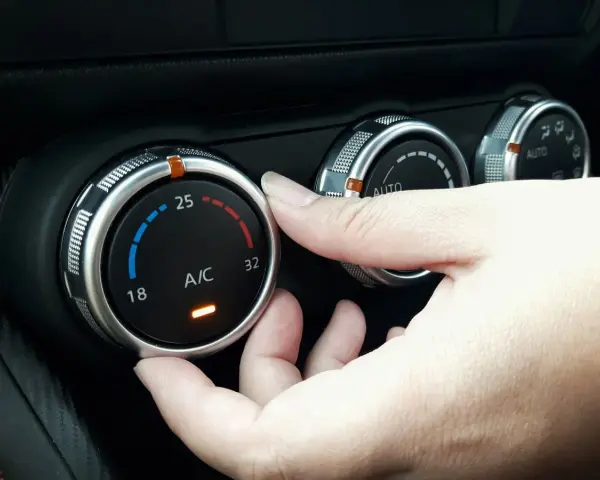 Dłoń reguluje pokrętłem temperaturę klimatyzacji w samochodzie, ustawiając ją na 25 stopni.