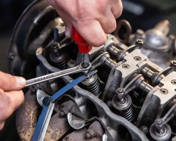 Mechanik reguluje luzy zaworowe silnika, używając klucza i szczelinomierza.