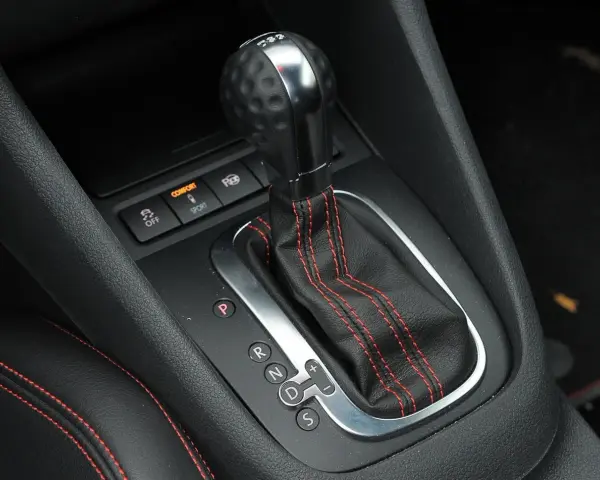 Zbliżenie na dźwignię automatycznej skrzyni biegów z oznaczeniami P, R, N, D, S. Widoczne przyciski trybów Comfort i Sport.