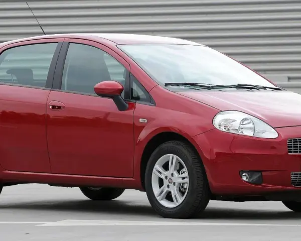 Czerwony Fiat Grande Punto, często chwalony w fiat grande punto opinie, stoi na szarym tle.