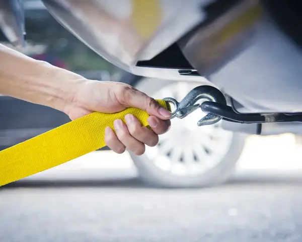 Dłoń mocuje żółtą linę holowniczą do haka. To kluczowy moment, jak holować auto, by bezpiecznie przetransportować pojazd.