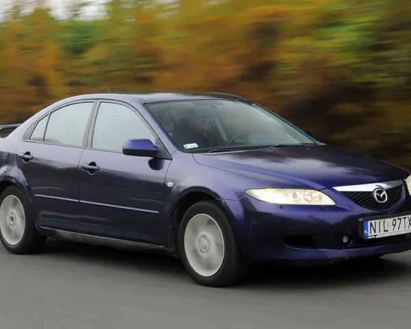 Granatowa Mazda 6 GG jedzie po drodze, za nią rozmyte drzewa w jesiennych barwach.