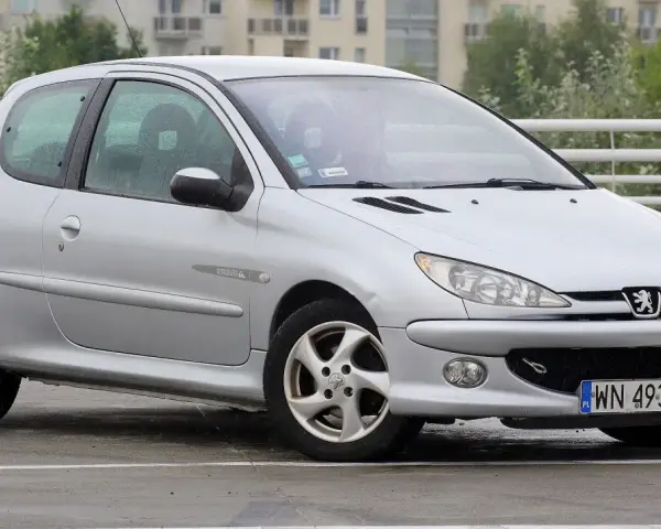 Srebrny Peugeot 206 Plus stoi na mokrym parkingu.