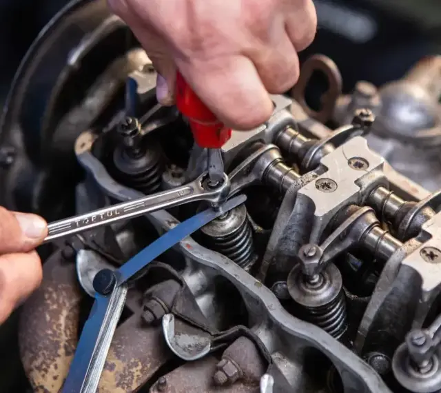 Mechanik reguluje luzy zaworowe silnika, używając klucza i szczelinomierza.
