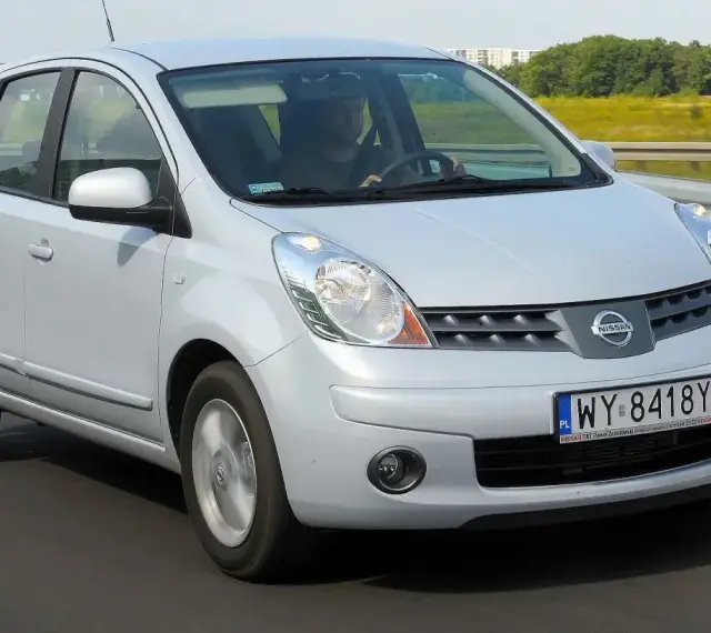 Srebrny Nissan Note E11 jedzie po drodze, za kierownicą siedzi mężczyzna.