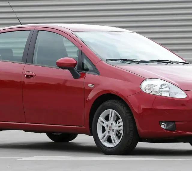 Czerwony Fiat Grande Punto, często chwalony w fiat grande punto opinie, stoi na szarym tle.
