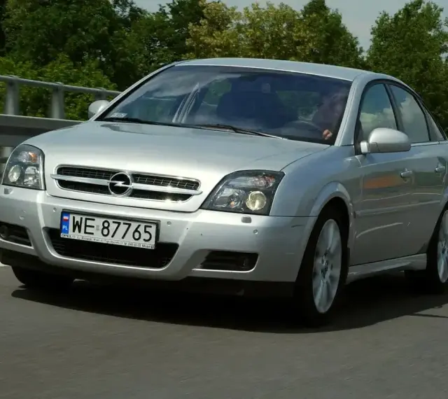 Srebrny Opel Vectra C GTS z polskimi tablicami WE 87765 jedzie po drodze, otoczony zielenią.