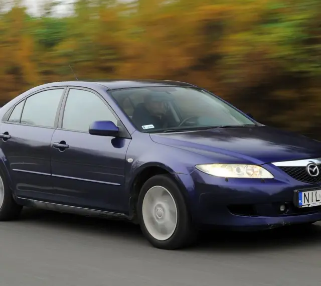 Granatowa Mazda 6 GG jedzie po drodze, za nią rozmyte drzewa w jesiennych barwach.