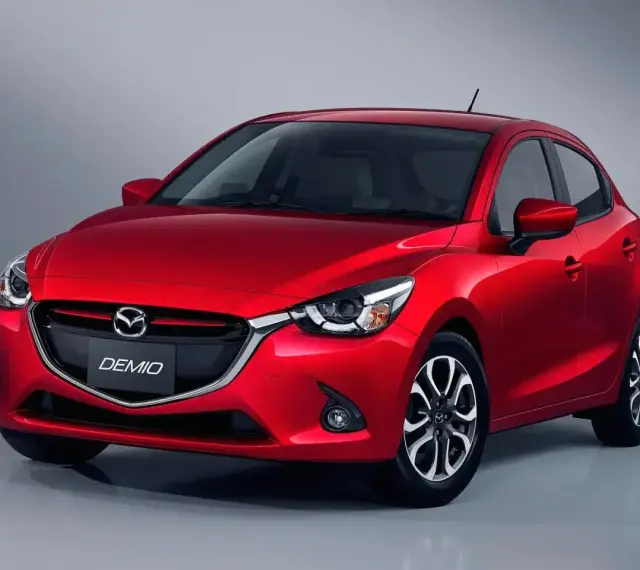 Czerwona Mazda Demio z błyszczącym grillem i reflektorami.