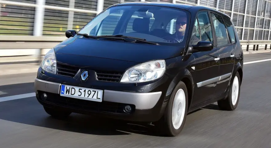 Czarny Renault Scenic 2 jedzie autostradą. Kierowca w okularach przeciwsłonecznych prowadzi auto.