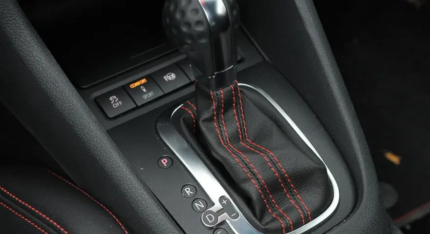 Zbliżenie na dźwignię automatycznej skrzyni biegów z oznaczeniami P, R, N, D, S. Widoczne przyciski trybów Comfort i Sport.