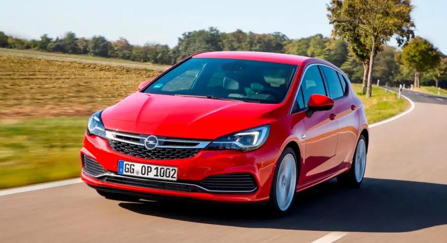 Czerwony Opel Astra jedzie po krętej drodze. W tle pola i drzewa. Idealny do diagnostyki z **op-com opel po polsku**.