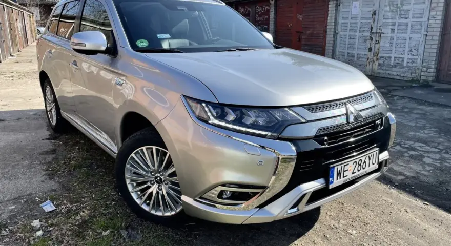 Srebrny Mitsubishi Outlander PHEV na tle garaży. Wiele osób szuka mitsubishi outlander opinie przed zakupem.