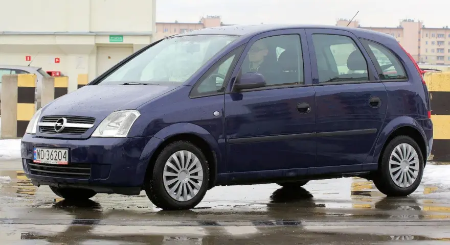 Granatowy Opel Meriva na mokrej nawierzchni. Kierowca w okularach. Wiele pozytywnych opinii o tym modelu.