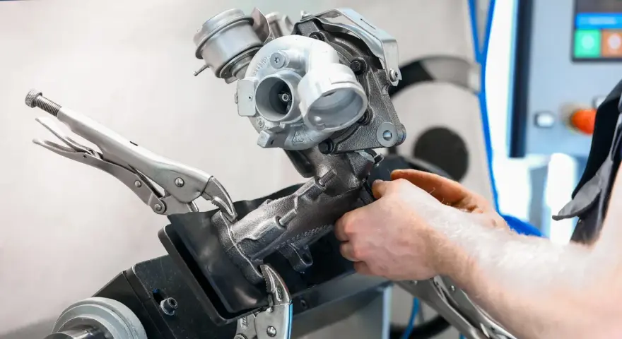 Mechanik naprawia turbosprężarkę, mocując ją imadłem. Widoczny jest zawór N75, kluczowy element sterujący.