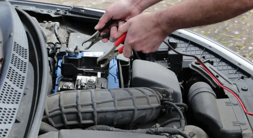 Ręce podłączają kable rozruchowe do akumulatora, bo auto nie odpala.