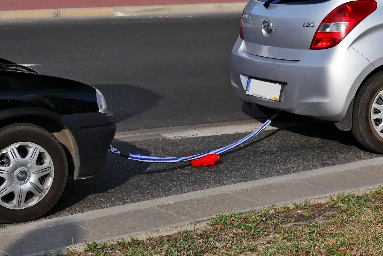 Czarny i srebrny samochód połączone liną holowniczą. Widać, jak holować auto, gdy jedno z nich uległo awarii.