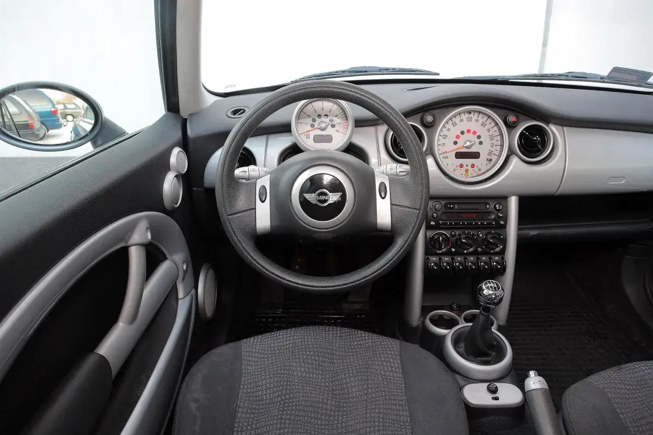 Wnętrze klasycznego mini r50: kierownica, deska rozdzielcza z okrągłymi zegarami, radio i dźwignia zmiany biegów.