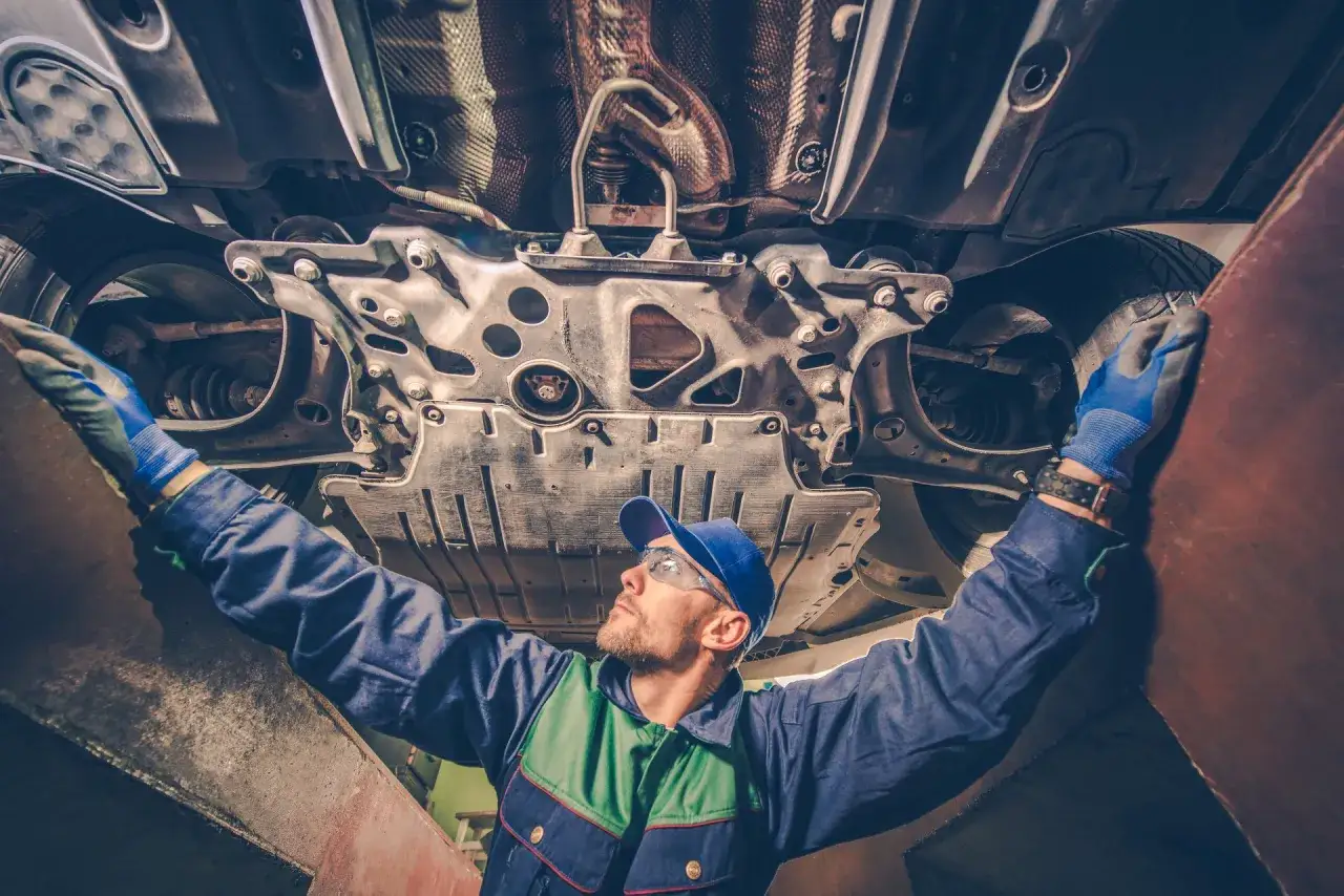 Mechanik w okularach i rękawiczkach sprawdza podwozie auta. Warto przeczytać kamoka opinie przed zakupem części.