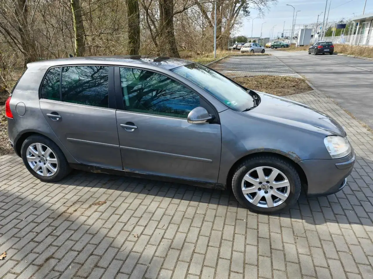 Szary Golf 4 1.4 16v stoi na parkingu. Widać odbicie drzew w przyciemnianych szybach.