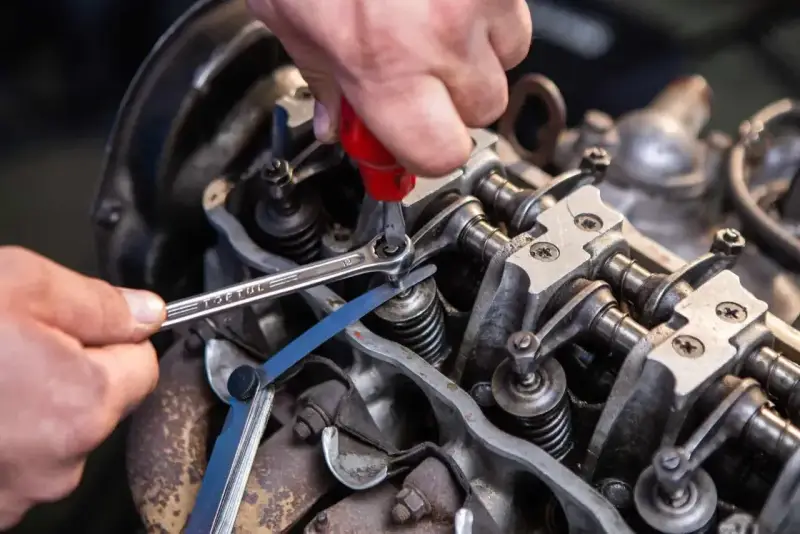 Mechanik reguluje luzy zaworowe silnika, używając klucza i szczelinomierza.