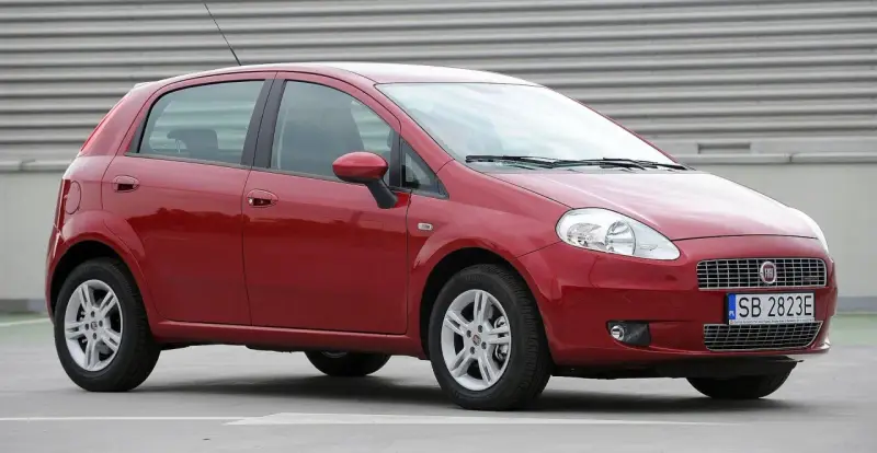 Czerwony Fiat Grande Punto, często chwalony w fiat grande punto opinie, stoi na szarym tle.
