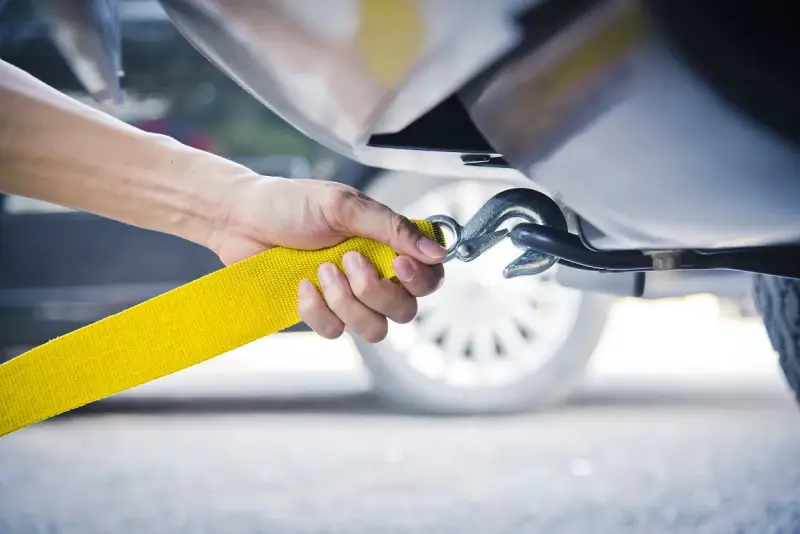 Dłoń mocuje żółtą linę holowniczą do haka. To kluczowy moment, jak holować auto, by bezpiecznie przetransportować pojazd.