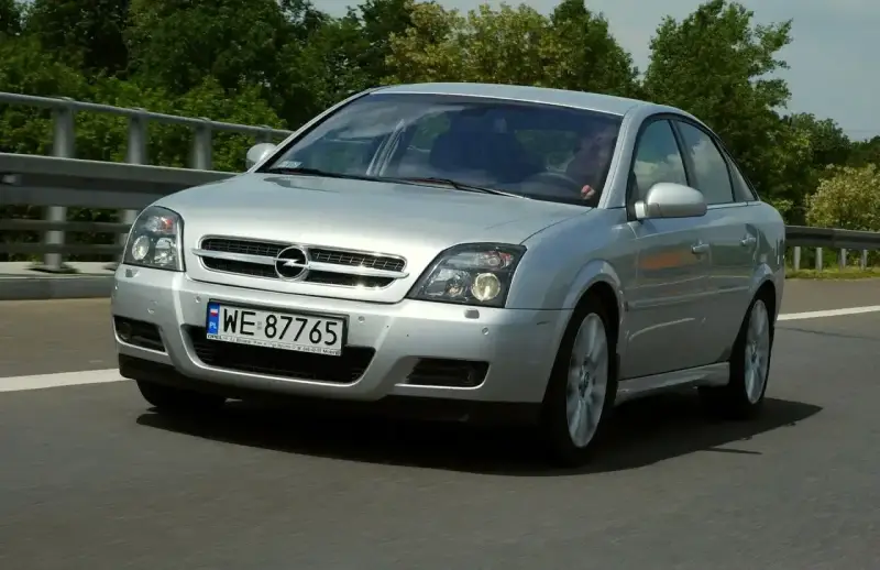 Srebrny Opel Vectra C GTS z polskimi tablicami WE 87765 jedzie po drodze, otoczony zielenią.