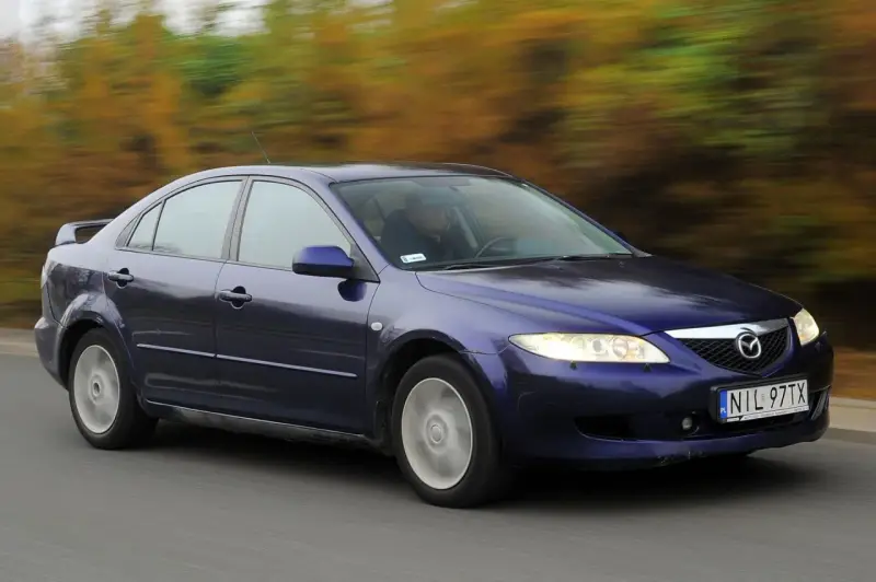 Granatowa Mazda 6 GG jedzie po drodze, za nią rozmyte drzewa w jesiennych barwach.